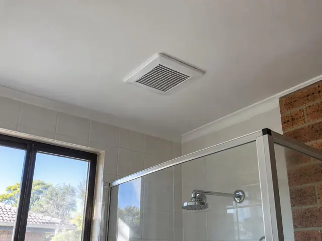 Ceiling exhaust vent above a tiled shower in a bathroom with a window and brick wall in Macquarie Park
