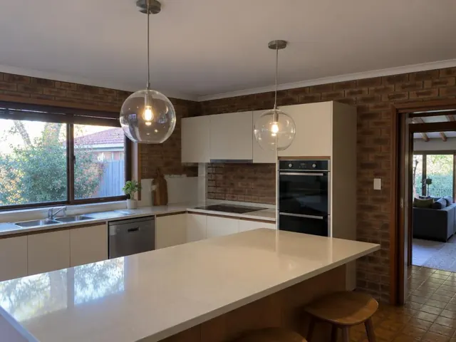 Modern kitchen with two glass pendant lights over a large island, brick feature wall and tiled floor in Macquarie Park